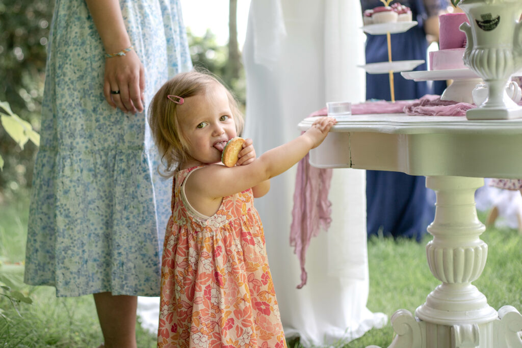 petite fille gourmande, qui pique un biscuit sur la table du salon de thé en extérieur